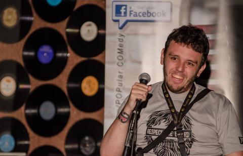 Richie pictured from the waist up holding a microphone and smiling, to his left are vinyl records stuck on a wall