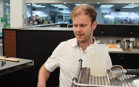 Harrison pictured working behind the coffee machine at his cafe. He is looking down at the coffee machine and wearing a white button up shirt.