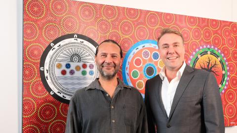 Chad and Rhys standing in front of CPL's Reconciliation Action Plan artwork hung on a wall