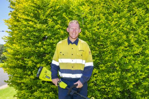Picture of Scott in yellow hi vis, stood in front of a hedge. 