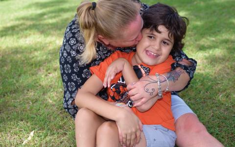 A mother and child are hugging each other and sitting on grass